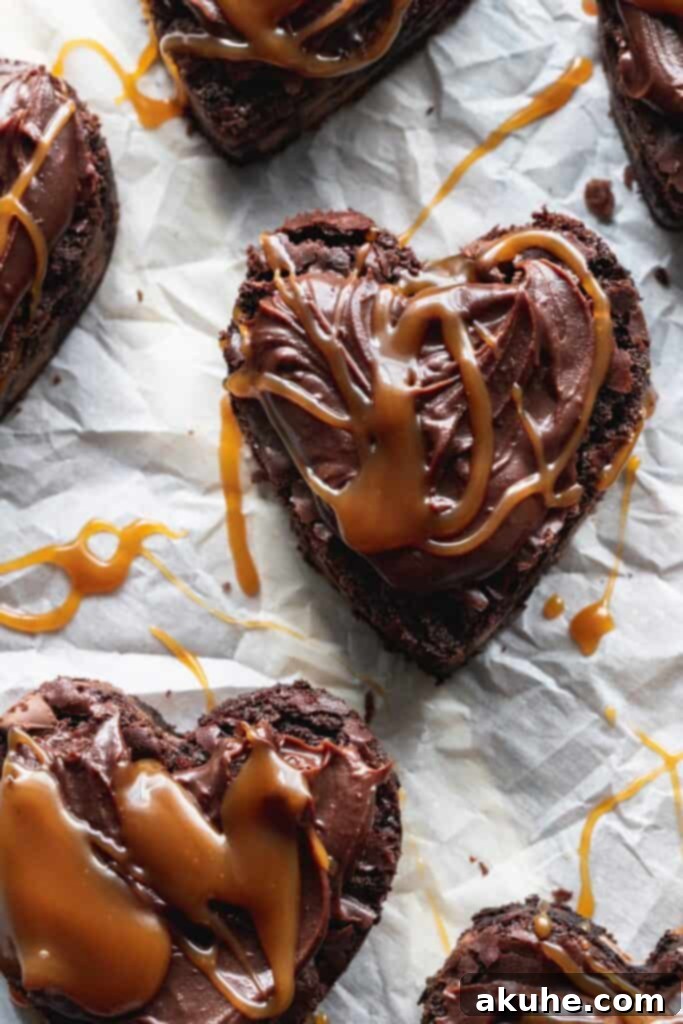 Close up of a moist, fudgy heart-shaped brownie, glistening with chocolate ganache and a swirl of salted caramel, ready to be enjoyed.