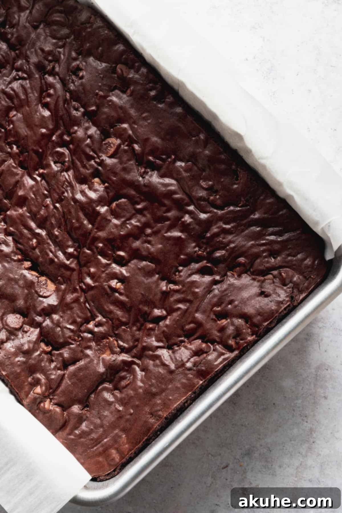 Freshly baked brownies, still warm in a silver baking pan, showing the signature crinkly top and set edges.
