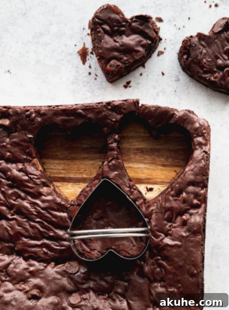 A hand using a heart-shaped cookie cutter to neatly cut out individual brownies from a larger baked slab on a cutting board.