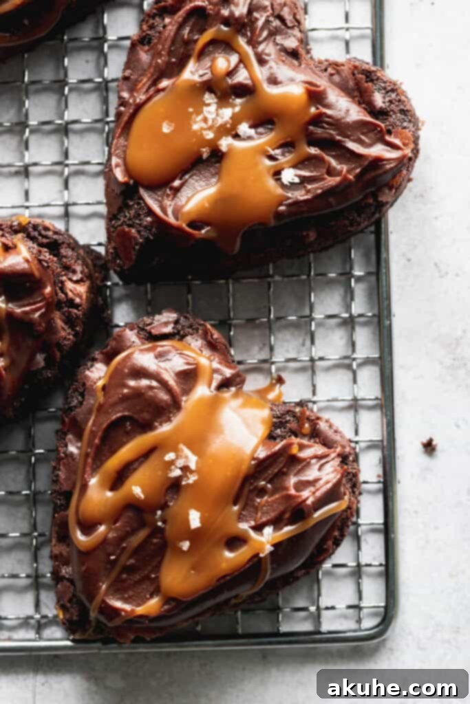A collection of heart-shaped brownies, freshly frosted with chocolate ganache, cooling on a wire rack.