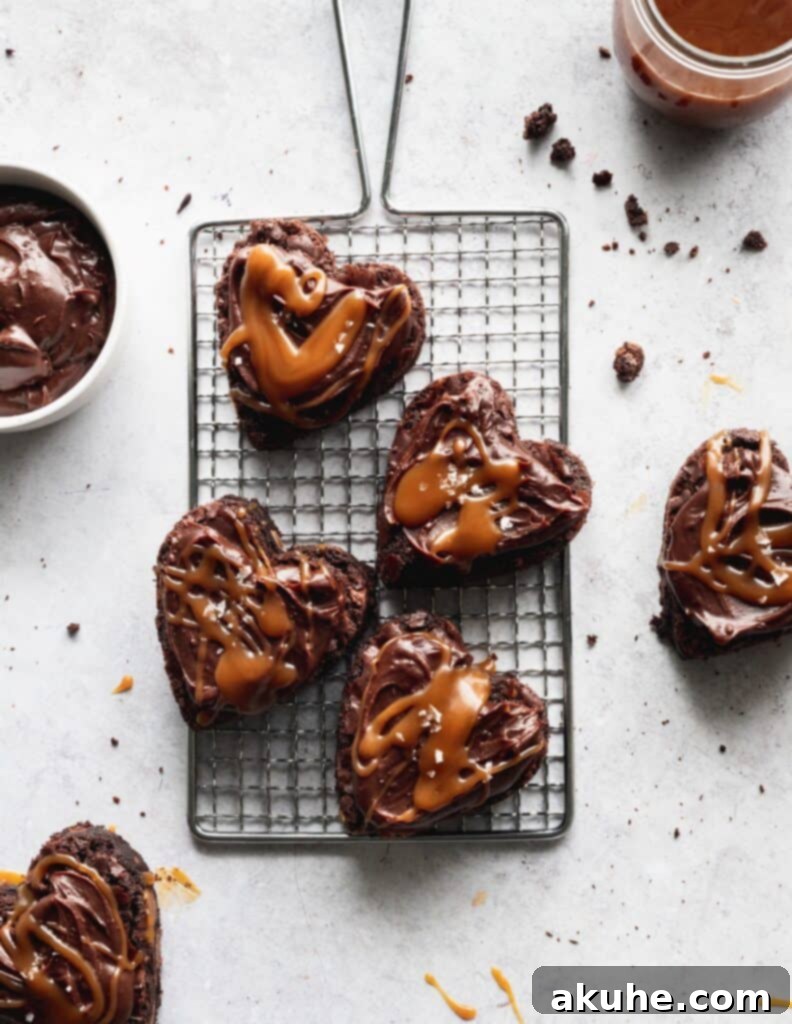 A close-up of several heart-shaped brownies, frosted and drizzled with caramel, arranged on a wire rack.