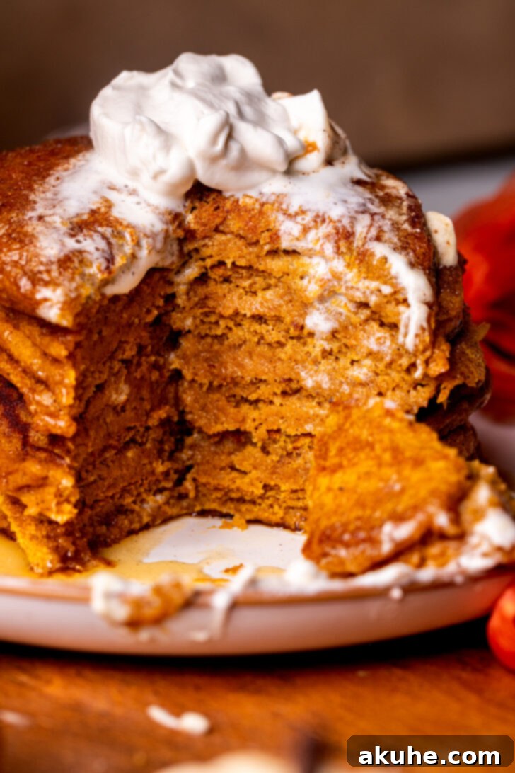 Warm Spiced Pumpkin Pancakes 2 Stack of golden-brown fluffy pumpkin pancakes on a plate, drizzled with maple syrup and a dollop of whipped cream.