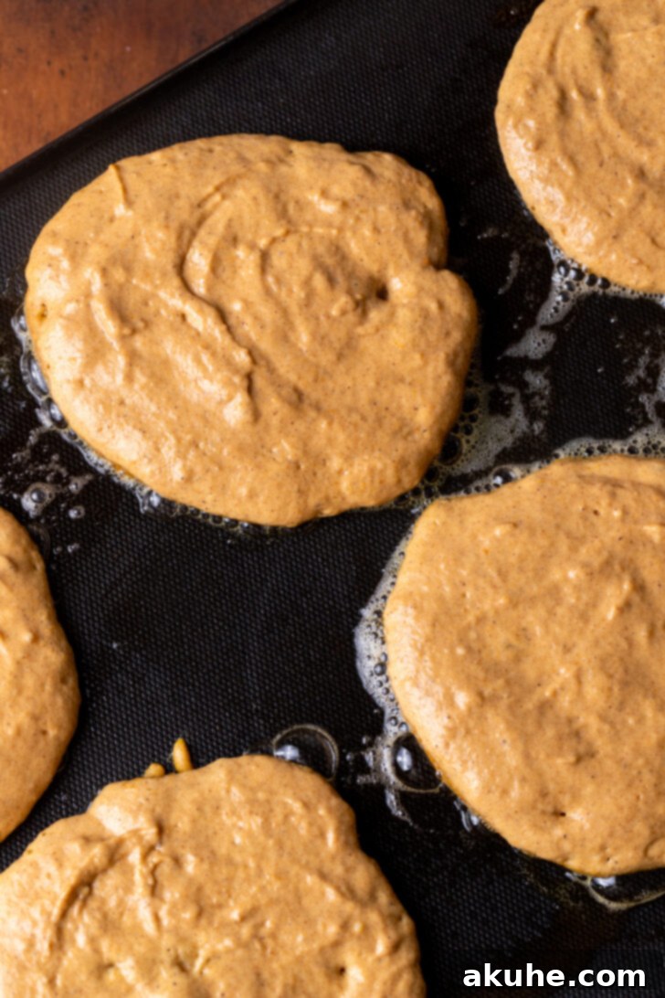 Warm Spiced Pumpkin Pancakes 6 Pancake batter cooking on a griddle, surrounded by melted butter.