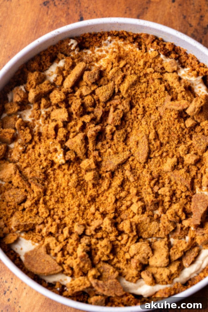 Half of the cheesecake batter spread over the crust, with crushed gingersnap crumbs sprinkled on top.
