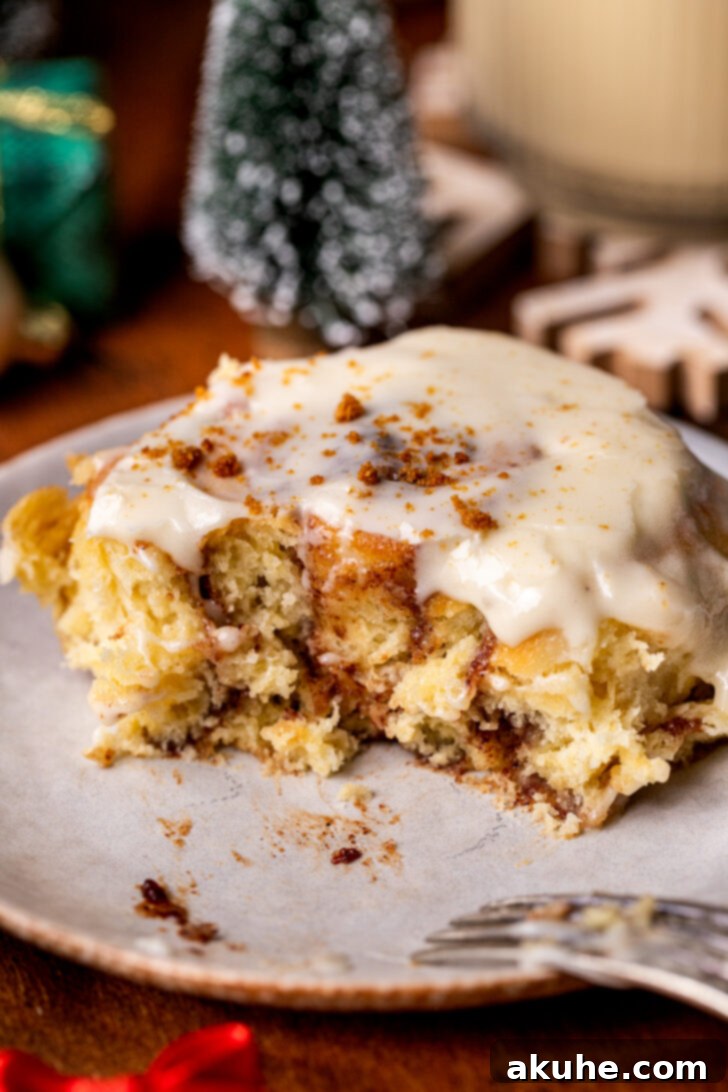 Festive Eggnog Swirls 3 One eggnog cinnamon roll on a plate, with a bite taken, revealing the soft interior and cinnamon swirl.