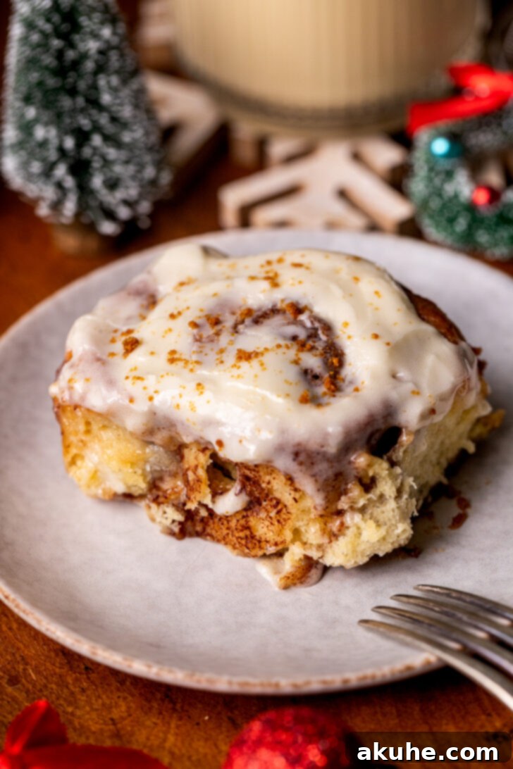 Festive Eggnog Swirls 10 A single eggnog cinnamon roll, beautifully iced and presented on a white plate, highlighting its festive appeal.