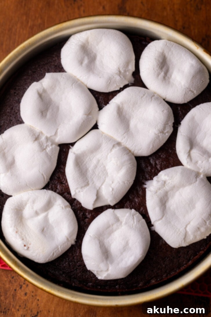 Melted marshmallows being gently pressed down on a cake layer.