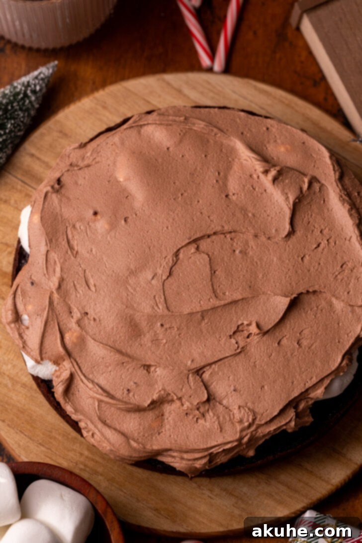 Hot chocolate frosting being spread on a cake layer with melted marshmallows.