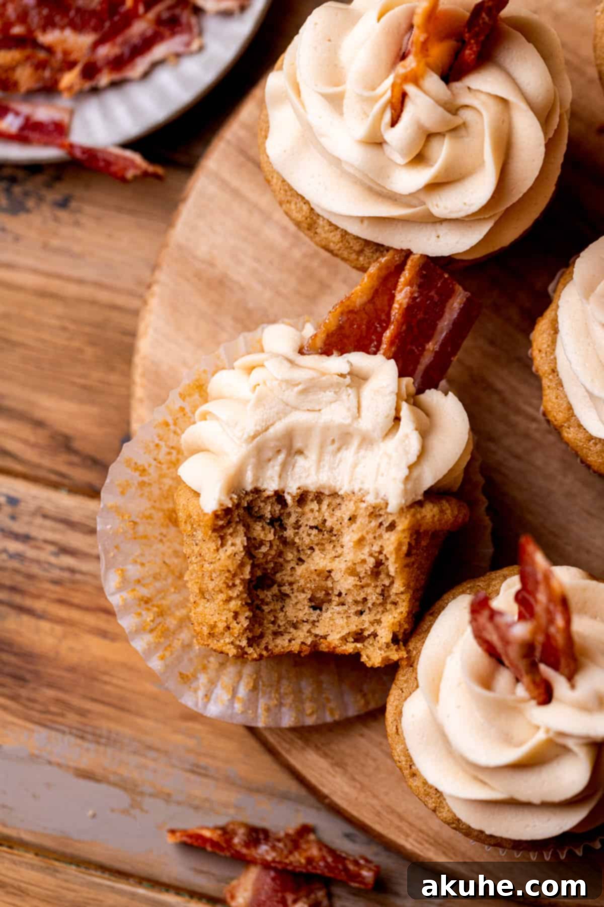 Maple Bacon Bliss Cupcakes 2 A beautifully frosted maple bacon cupcake with a bite taken out, showcasing the fluffy cake and crispy candied bacon topping.