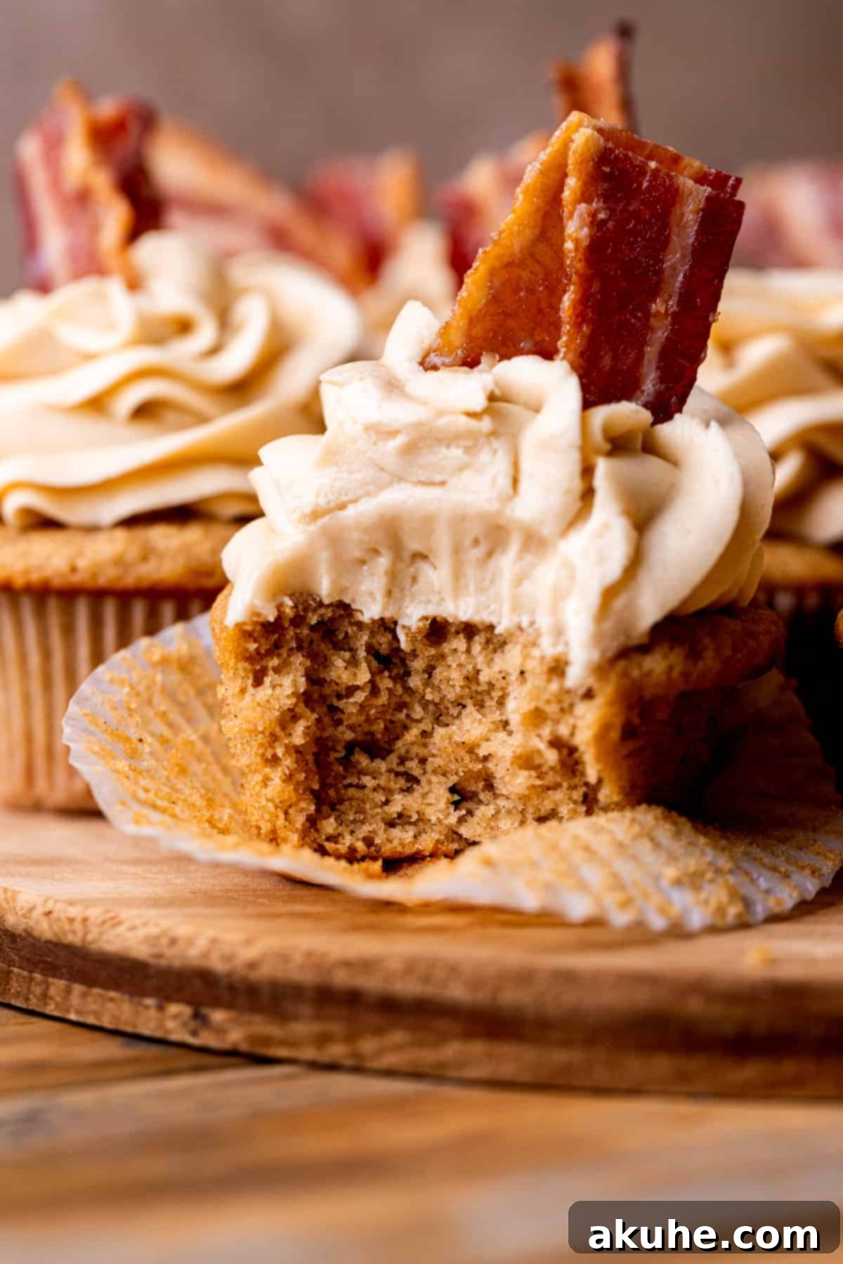Maple Bacon Bliss Cupcakes 11 A close-up view of a maple bacon cupcake with a bite missing, showing the moist cake, creamy frosting, and crunchy bacon.