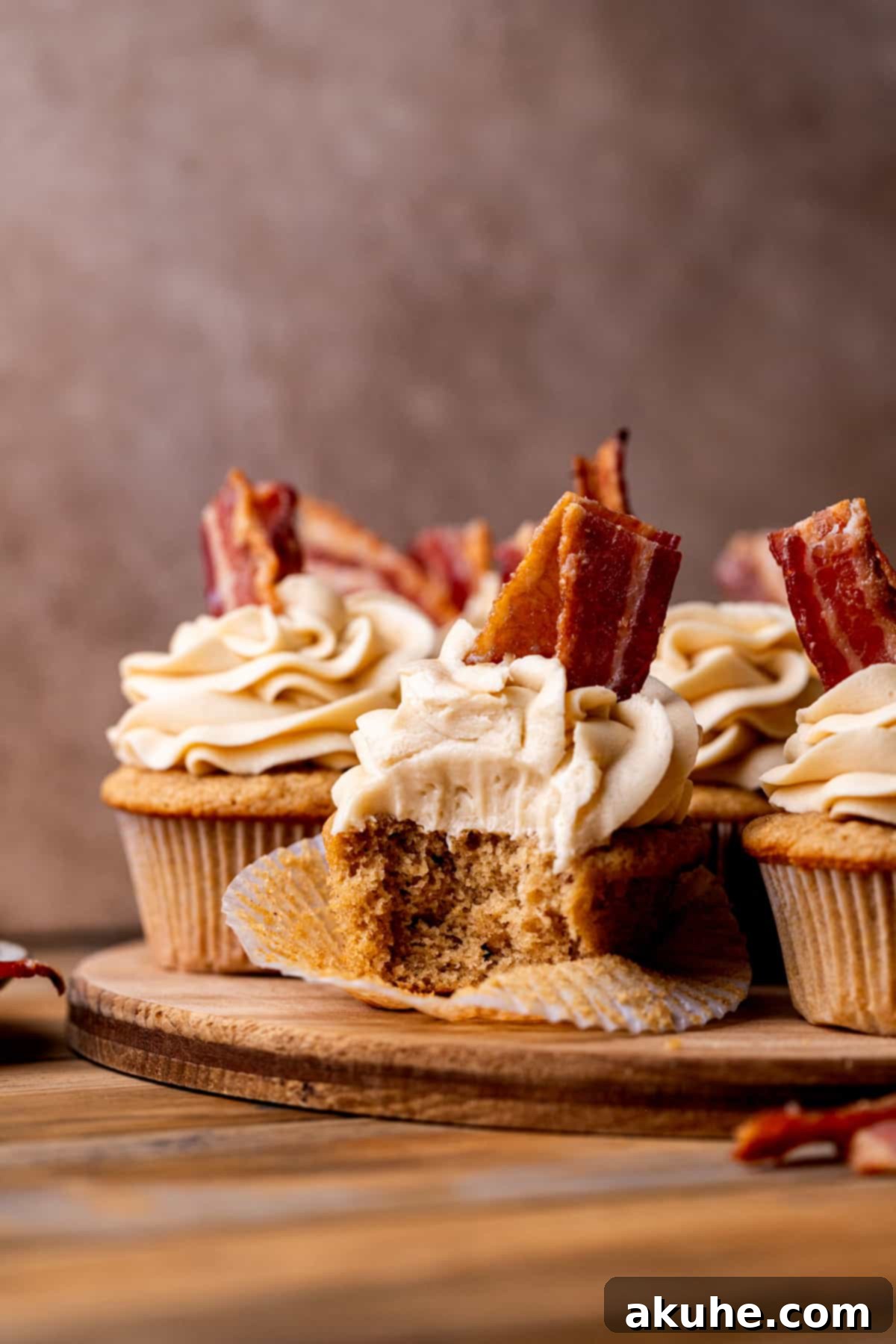 Maple Bacon Bliss Cupcakes 3 A trio of beautifully arranged maple bacon cupcakes on a rustic wooden board, ready to be enjoyed.