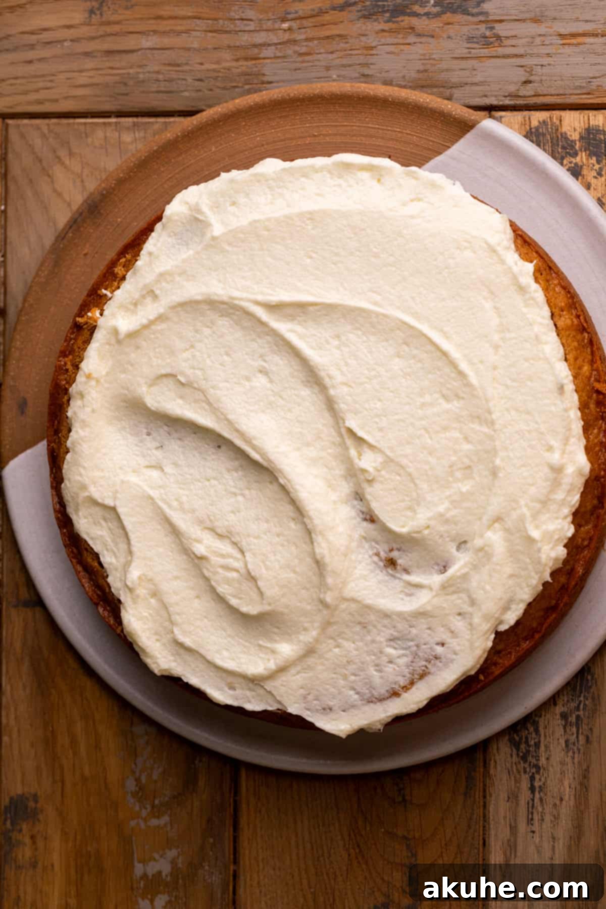 Heavenly Carrot Cake 8 A generous layer of smooth cream cheese frosting spread evenly on the first layer of a baked carrot cake.