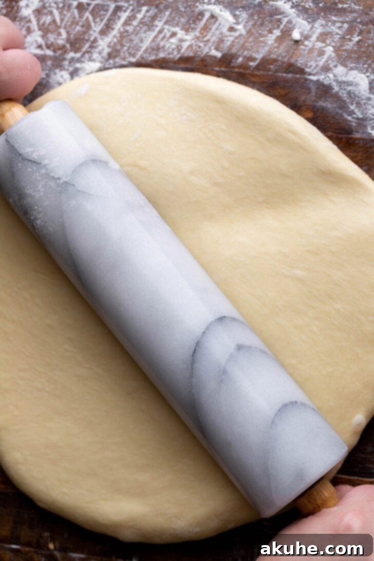Dough being rolled out on a lightly floured surface into a rectangular shape.