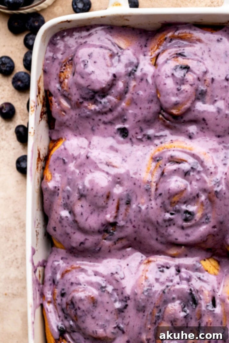 A top-down view of beautifully iced blueberry cinnamon rolls in a square pan, ready to be served.