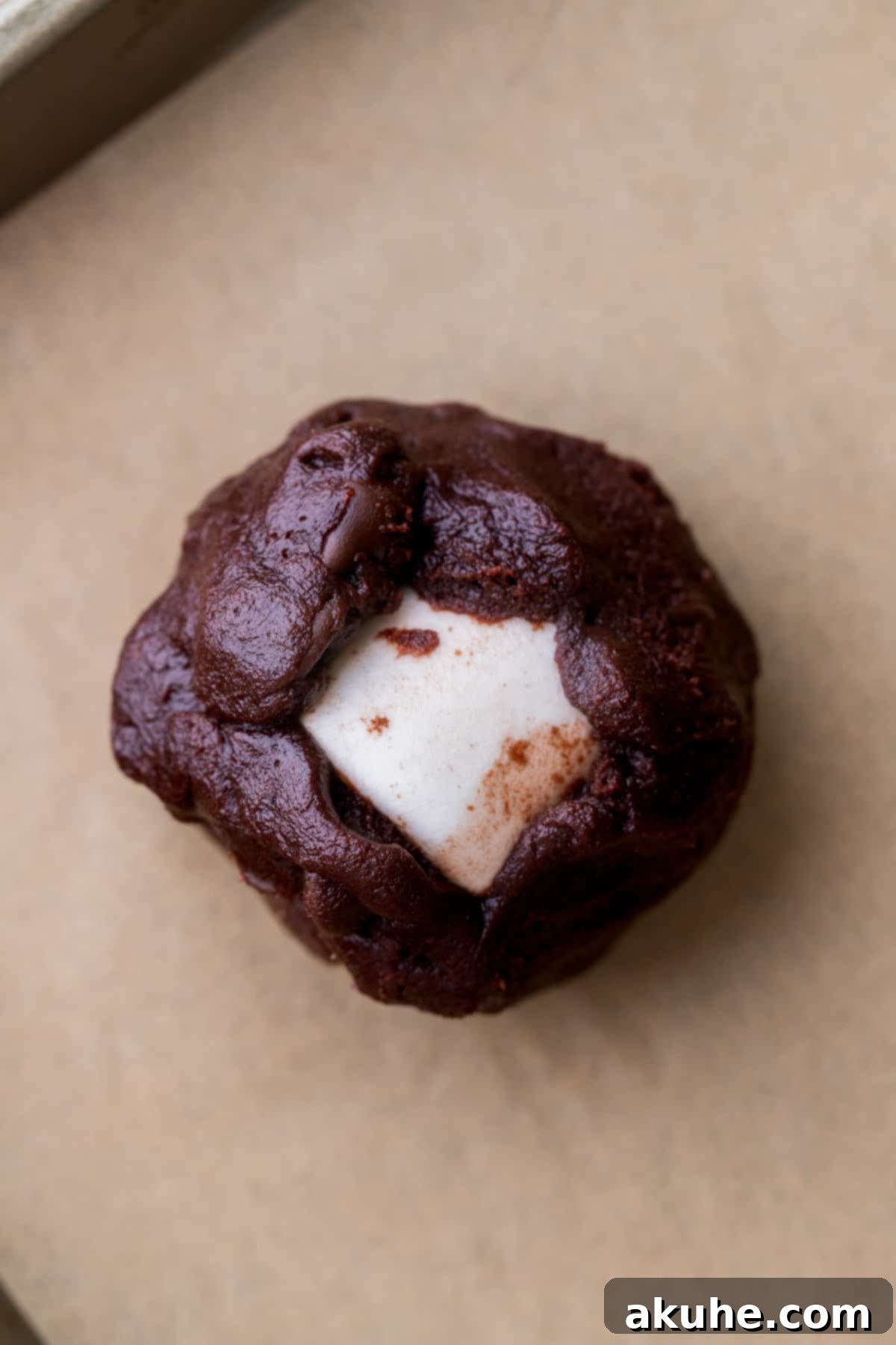 Cookie dough ball with marshmallow enclosed, placed on a cookie sheet.