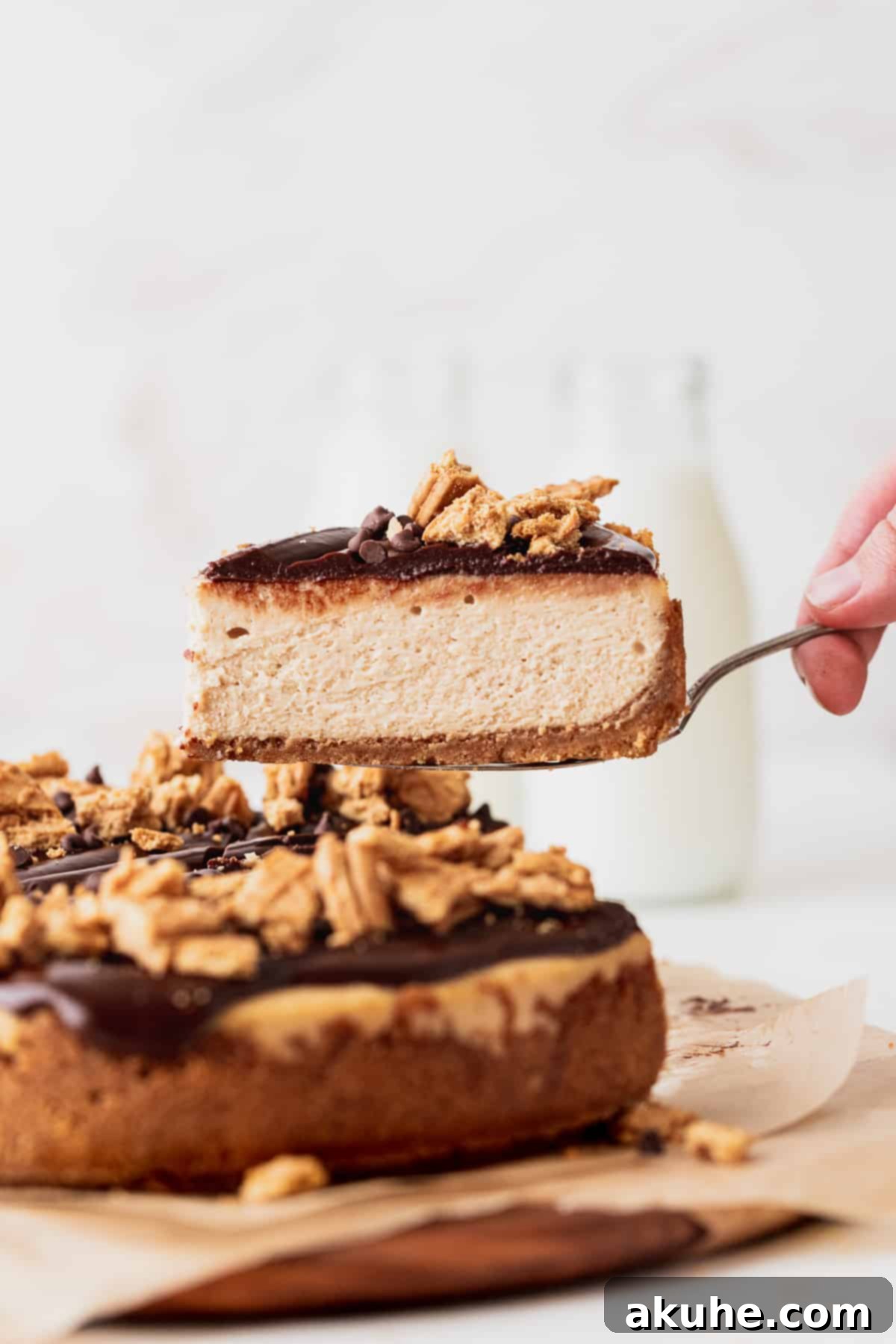 A hand gently pulling a slice of rich peanut butter cheesecake away from the main dessert.