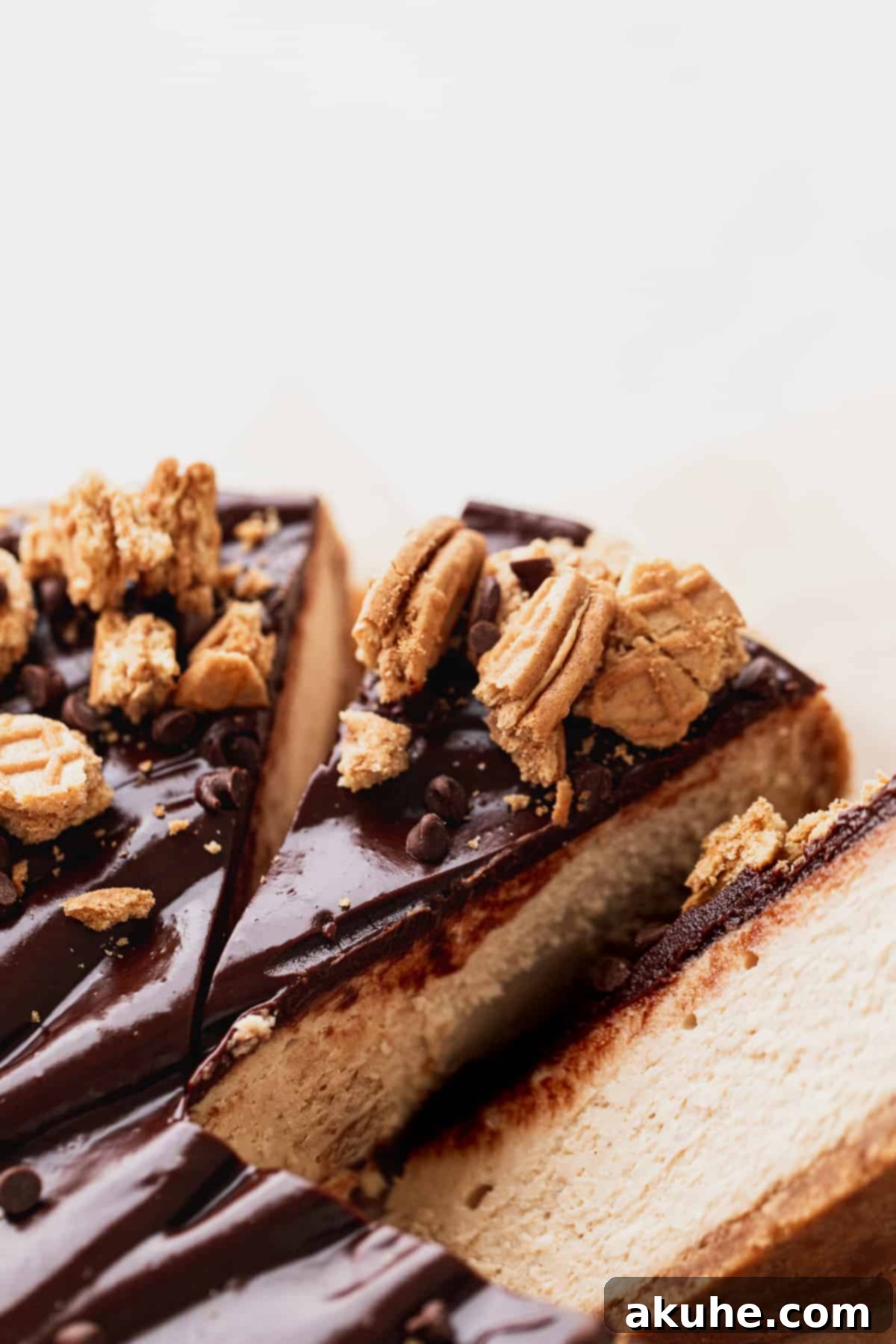 Close up of a perfect slice of peanut butter cheesecake on a white plate, showing the distinct layers of crust, filling, and ganache.