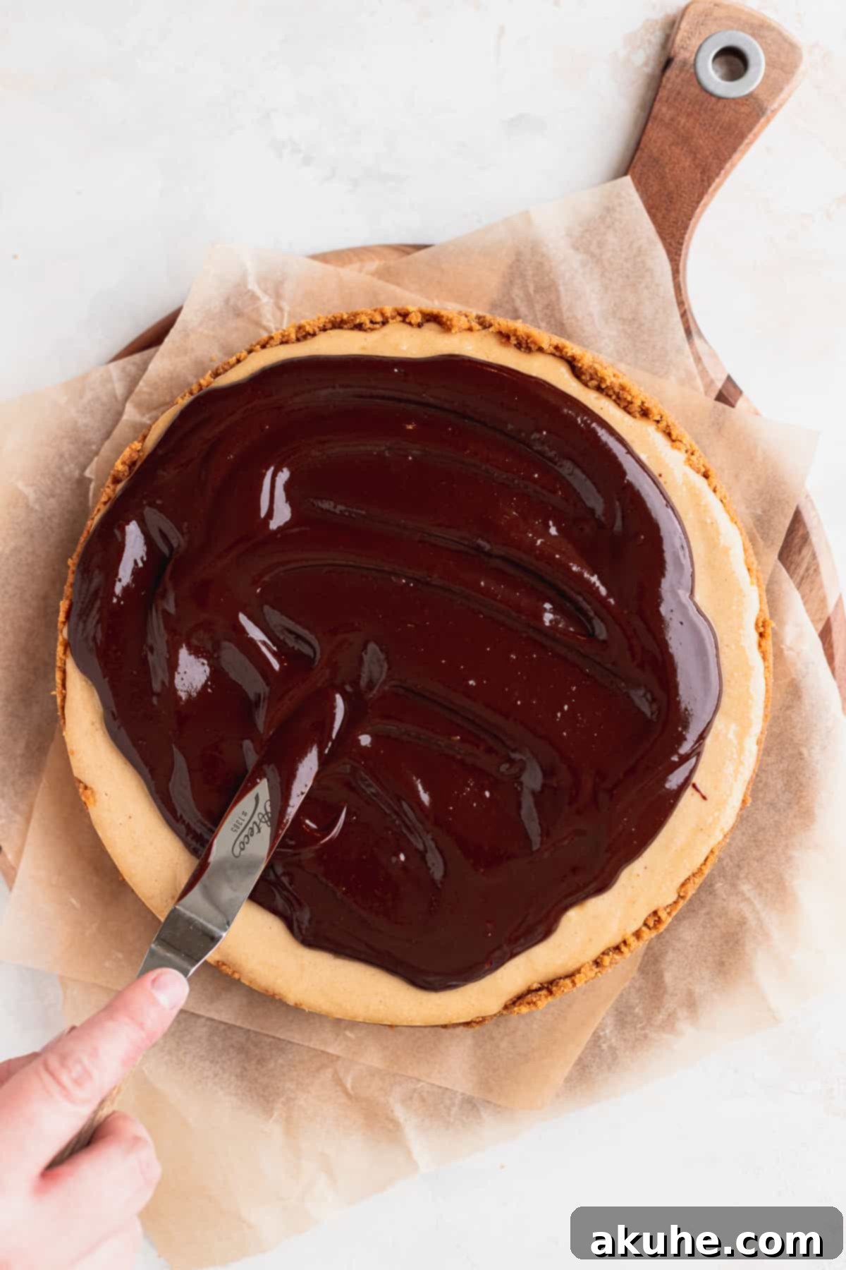 Smooth chocolate ganache being spread evenly over the chilled peanut butter cheesecake.