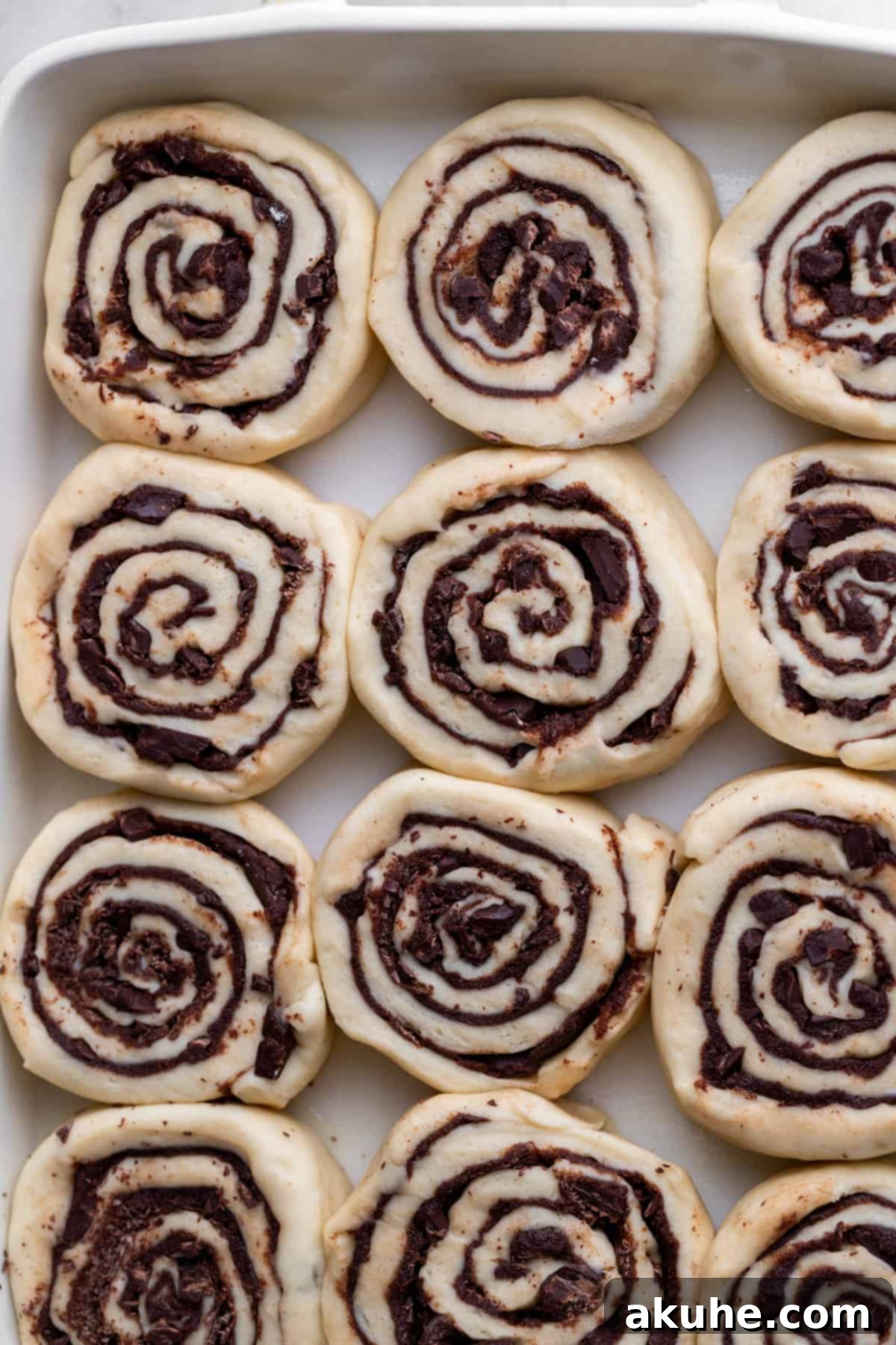 Chocolate Cinnamon Rolls 7 Unbaked chocolate cinnamon rolls arranged in a baking pan, ready for the oven.