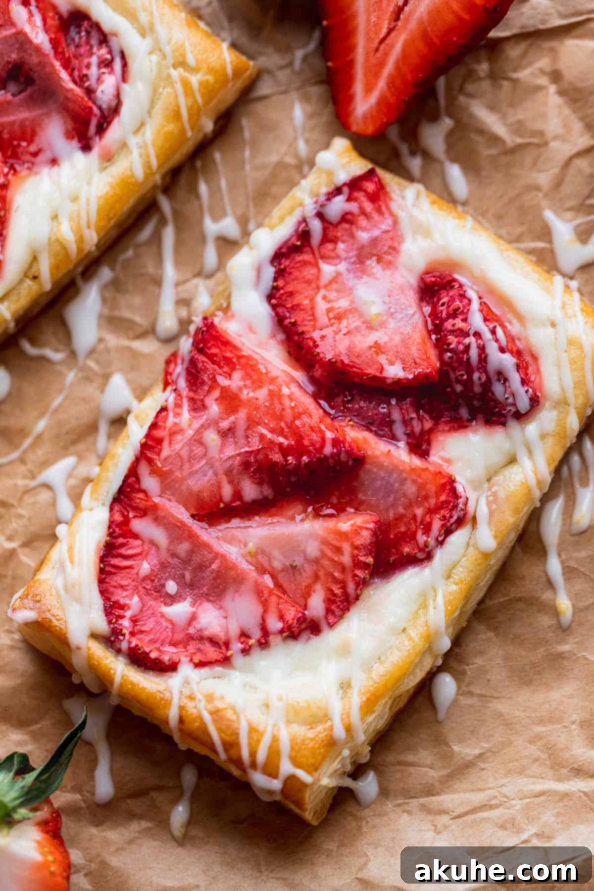 A close-up view of a baked Strawberry Danish, showcasing the vibrant fresh strawberries, creamy filling, and delicate lemon icing drizzle.
