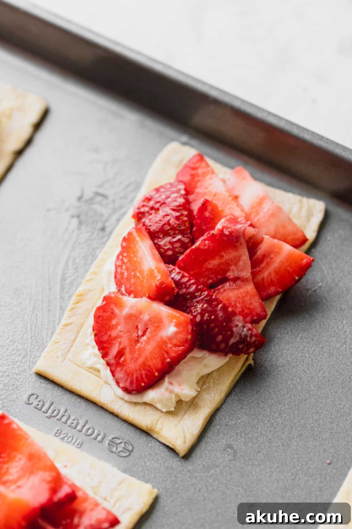 Fresh strawberry slices arranged neatly over cream cheese on puff pastry.