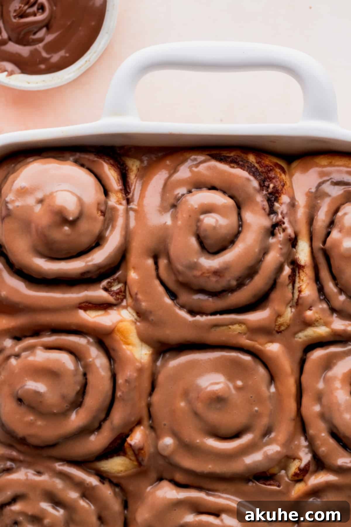 A batch of baked and iced Nutella rolls arranged neatly in a baking pan.