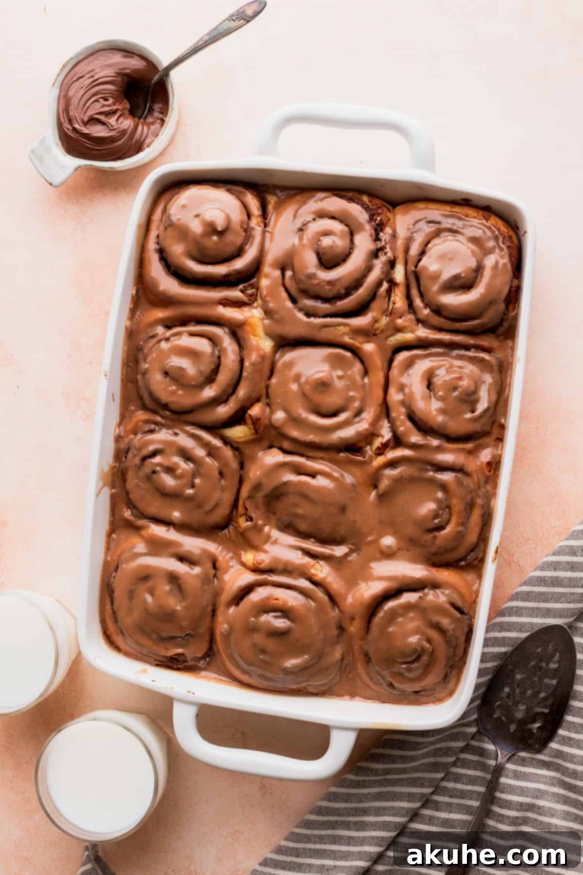 Freshly baked and iced Nutella rolls in a baking pan, next to a bowl of Nutella spread.