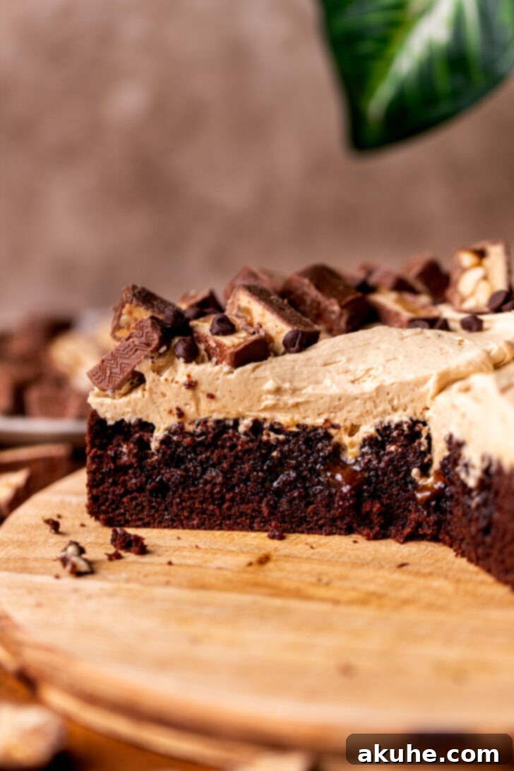 A beautiful side view of the Snickers cake, showing the thick layer of peanut butter frosting and chopped Snickers bars on top of the chocolate cake.