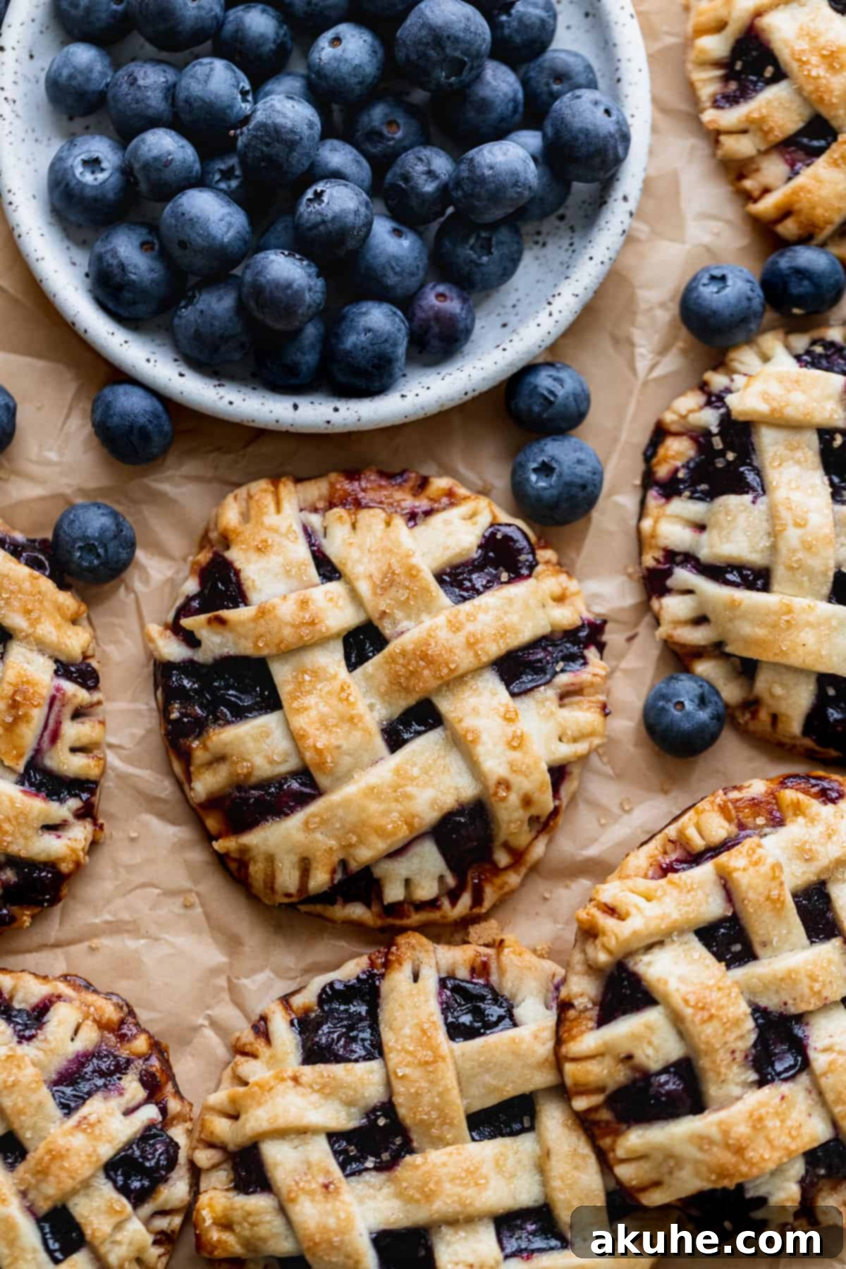 Blueberry Pie Bites 2 Close-up of golden brown mini blueberry pies with lattice tops, artfully arranged on a rustic plate, surrounded by fresh, vibrant blueberries.