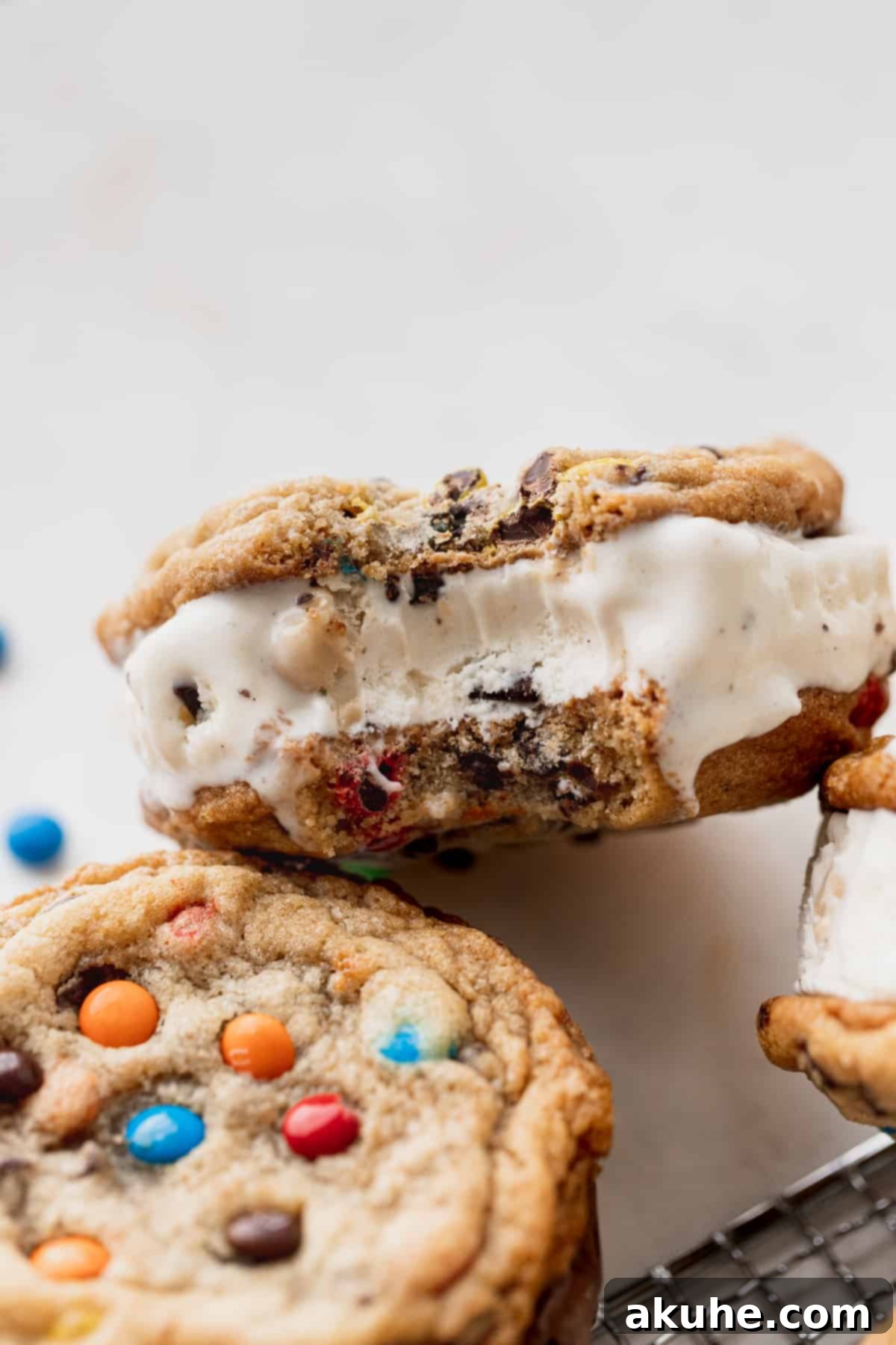 A perfectly assembled M&M cookie ice cream sandwich with a bite taken out, revealing the creamy layers of vanilla and chocolate ice cream between two colorful cookies.