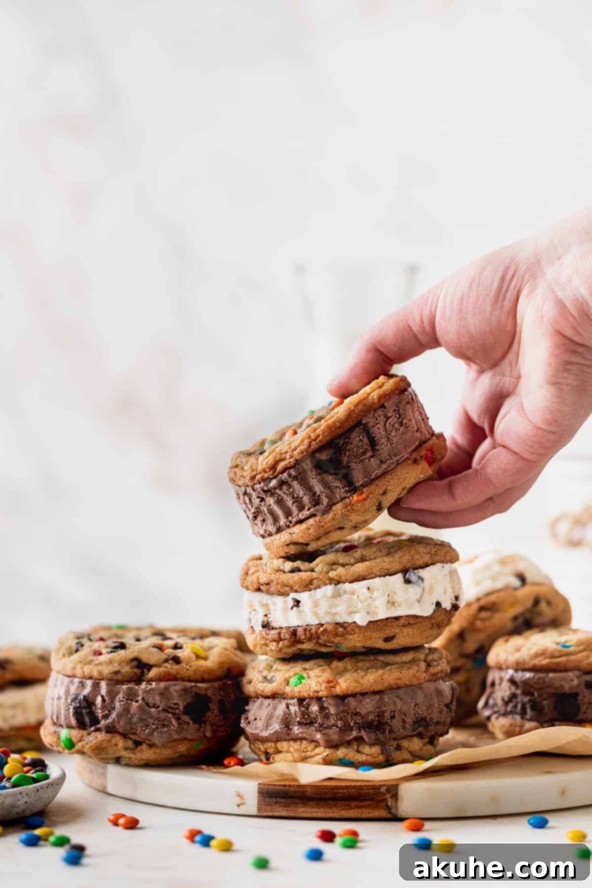 A hand gently lifting a freshly baked, large M&M cookie from a cooling rack, showcasing its soft texture and colorful candies.