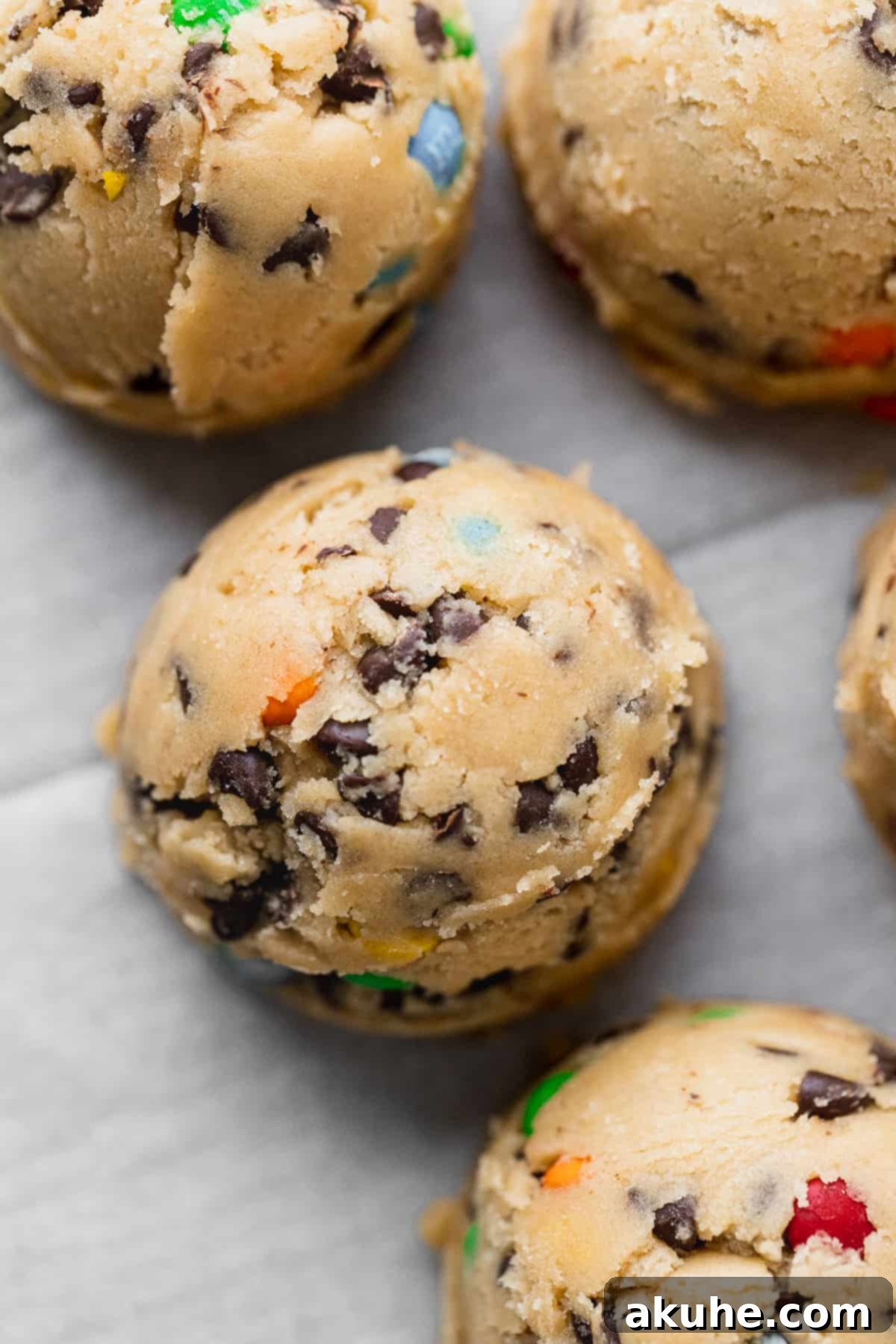 Portioned M&M cookie dough balls neatly arranged on a parchment-lined cookie sheet, ready for baking.