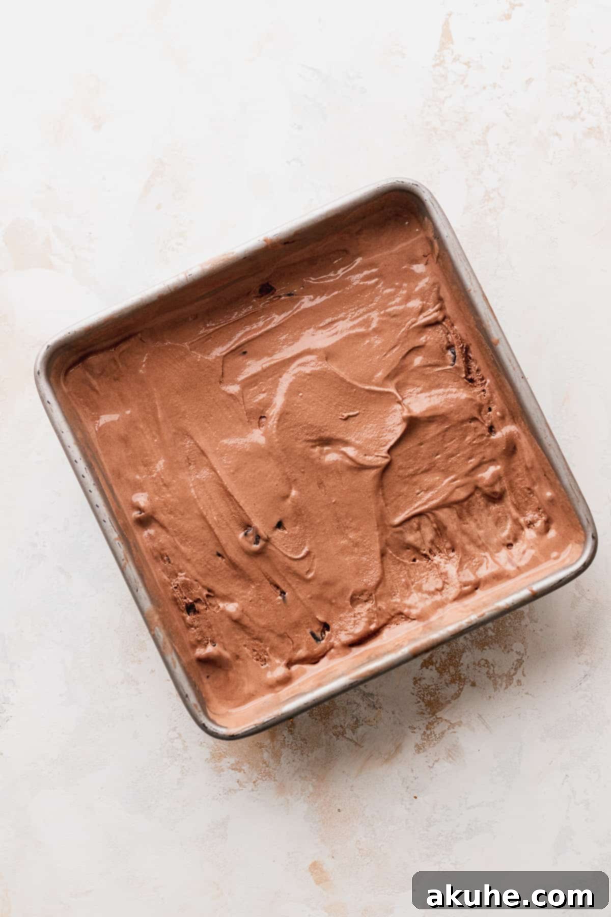 Smooth chocolate ice cream spread evenly in a metal tin, awaiting freezing and portioning.