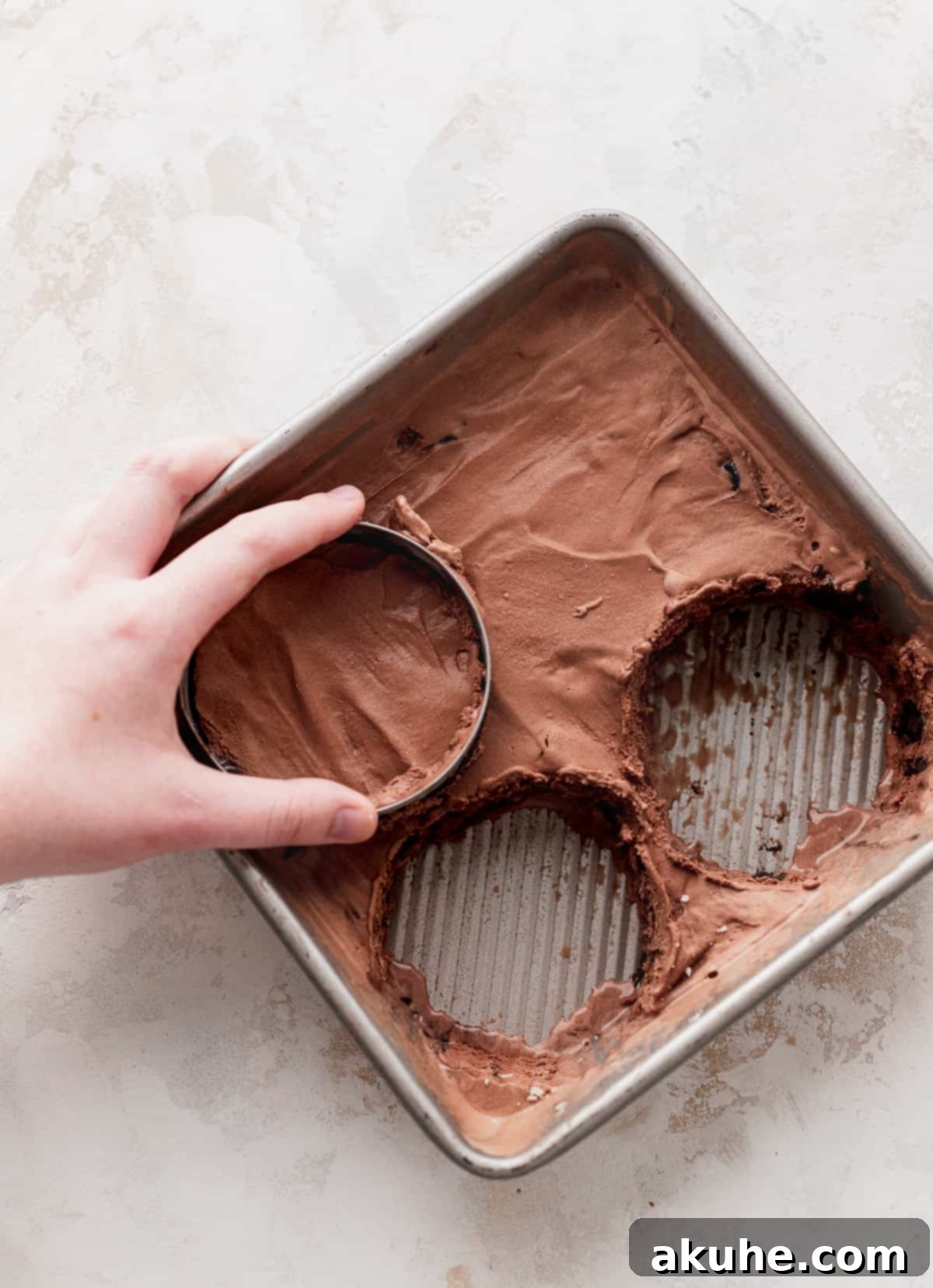 A biscuit cutter pressing a perfect circle into a frozen layer of chocolate ice cream, preparing for assembly into a sandwich.