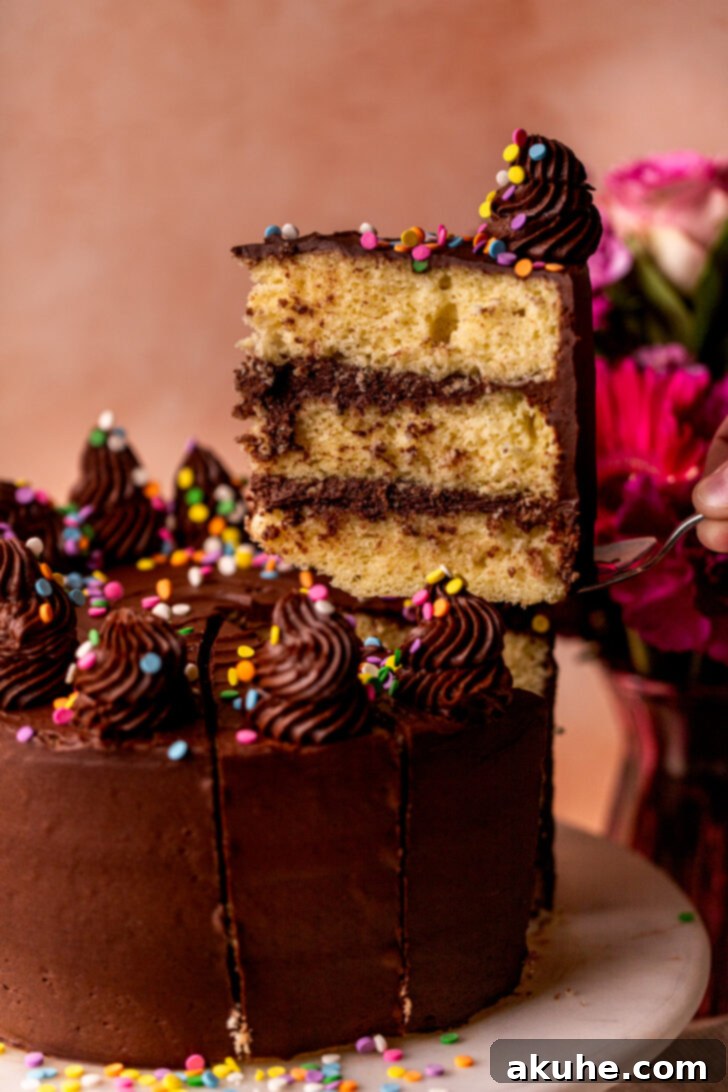 Classic Yellow Cake 2 A slice being carefully removed from a beautifully decorated three-layer homemade yellow cake, showcasing its moist texture and rich chocolate cream cheese frosting.