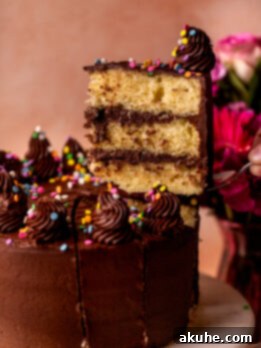 Classic Yellow Cake 13 A slice being carefully removed from a beautifully decorated three-layer homemade yellow cake, showcasing its moist texture and rich chocolate cream cheese frosting.