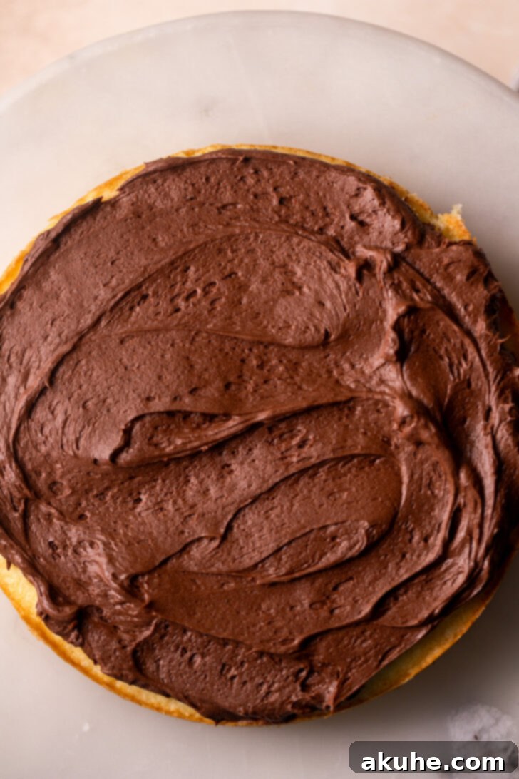 Classic Yellow Cake 8 A skilled hand spreading a generous layer of chocolate cream cheese frosting onto a yellow cake layer, ensuring even coverage.