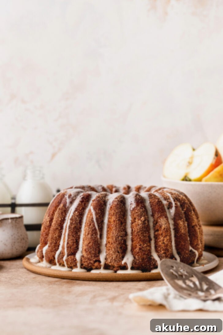 Spiced Apple Cider Donut Cake 8 A beautifully decorated apple cider donut cake, with its glaze dripping, presented on a rustic wooden board.