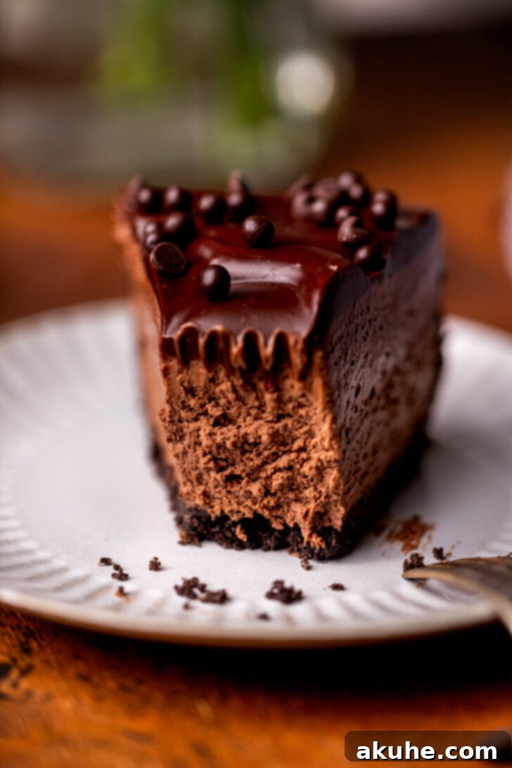 A close-up side view of a no-bake chocolate cheesecake slice with a bite missing, showcasing the thick, creamy chocolate filling and crunchy Oreo crust.