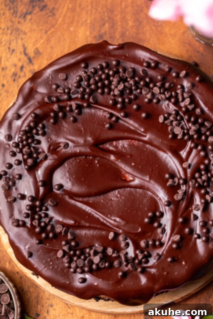 A fully decorated no-bake chocolate cheesecake, adorned with chocolate pearls and mini chocolate chips, presented on a rustic wooden board.