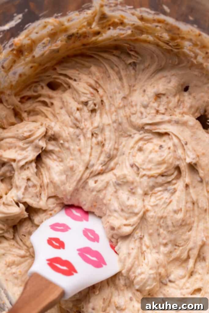 Decadent Butterfinger Crunch Cake 8 Butterfinger cream cheese frosting in a glass bowl, showing small, finely ground crumbs of Butterfinger mixed throughout.