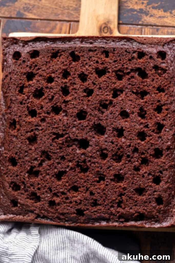 Decadent Butterfinger Crunch Cake 9 Baked chocolate cake with evenly spaced holes poked into its surface, ready for filling.