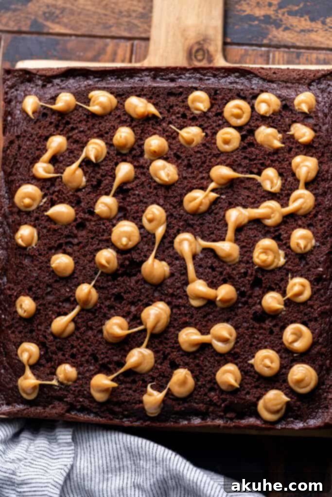 Decadent Butterfinger Crunch Cake 10 Peanut butter filling being piped into the poked holes of the chocolate cake, filling each cavity.