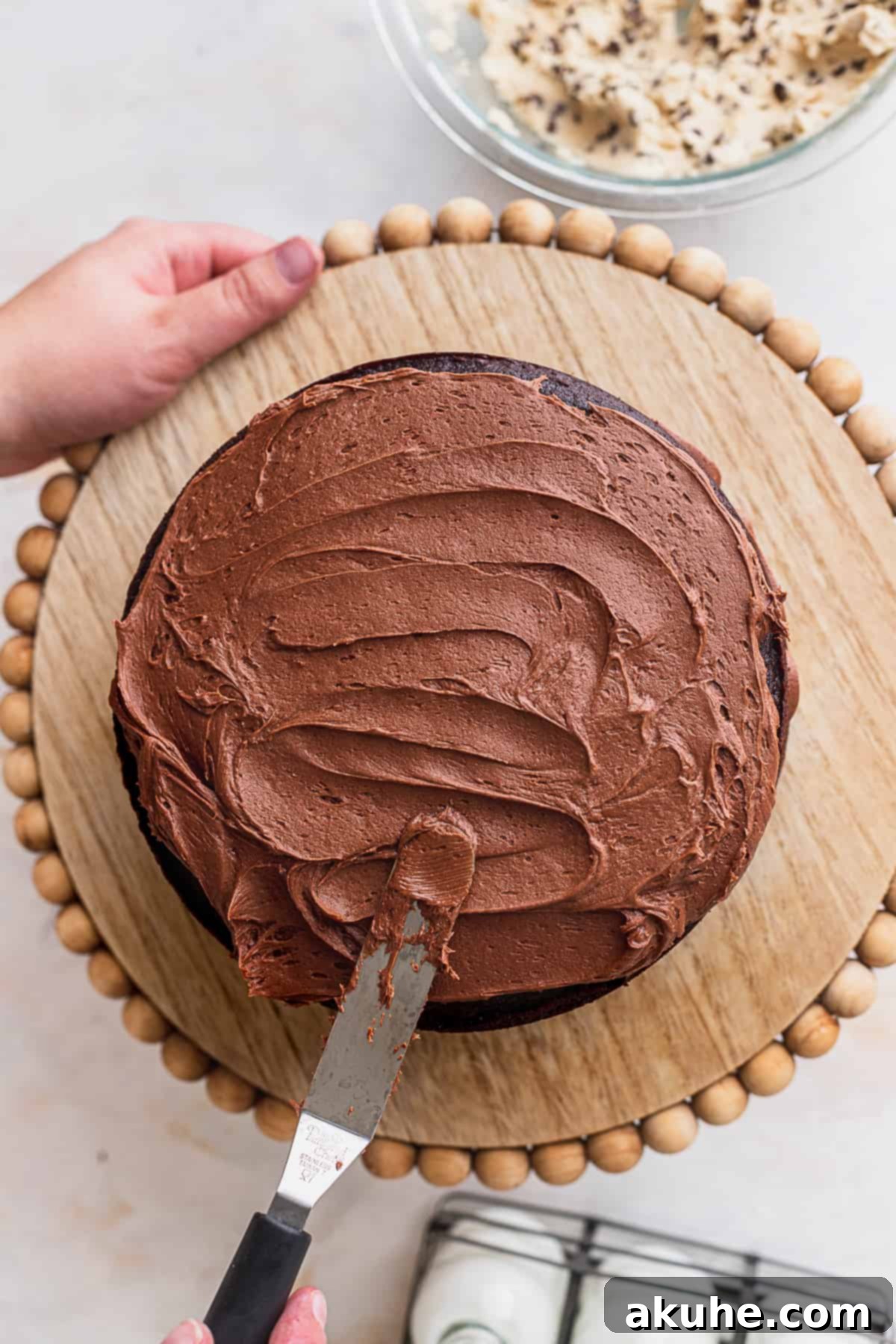 Decadent Cookie Brownie Cake 11 Spreading chocolate fudge frosting smoothly on top of a cake layer.
