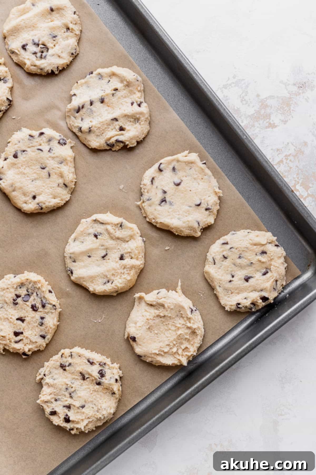 Decadent Cookie Brownie Cake 6 Flattened cookie dough discs arranged on a parchment-lined cookie sheet.