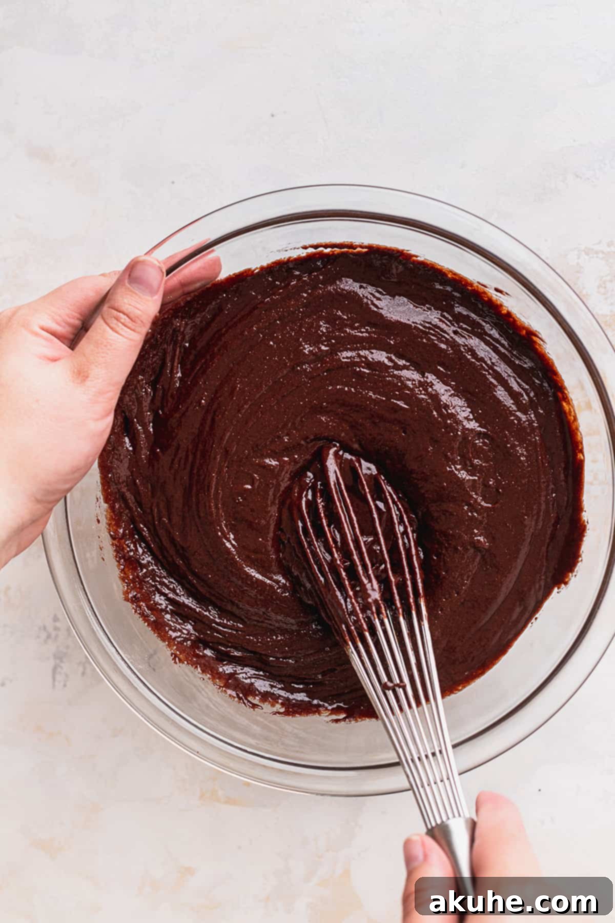 Decadent Cookie Brownie Cake 7 Mixing dark cake batter in a clear glass bowl.