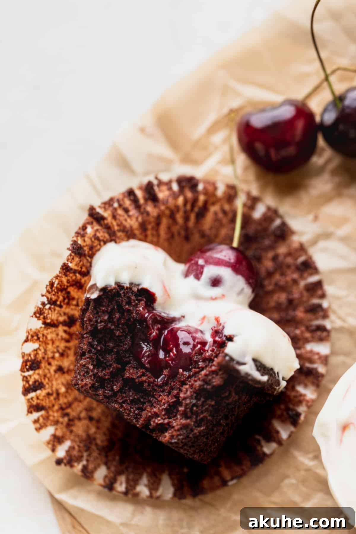 Decadent Black Forest Cupcakes 11 A Black Forest cupcake with a small bite taken out, revealing the moist chocolate cake and juicy cherry filling inside.