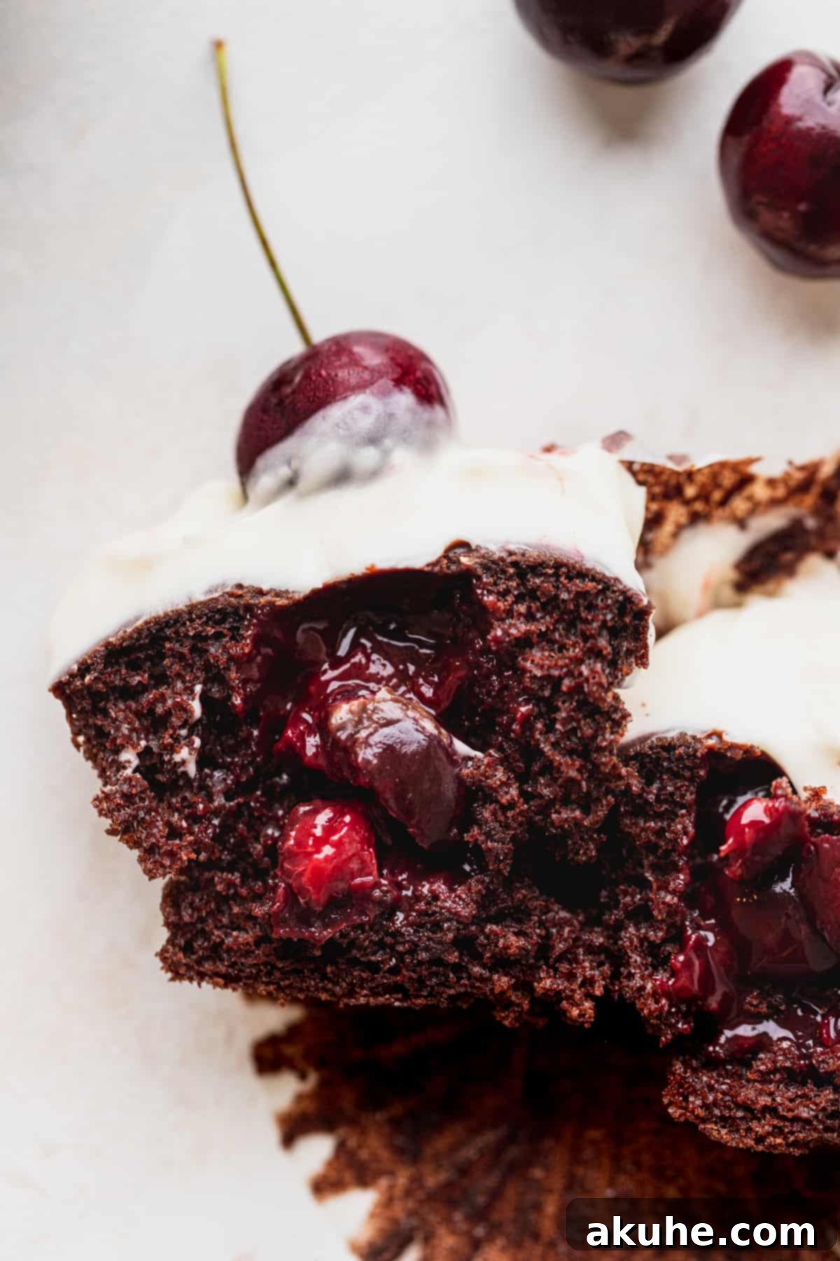 Decadent Black Forest Cupcakes 3 A Black Forest cupcake elegantly split in half, revealing its moist chocolate cake, vibrant red cherry filling, and the soft whipped cream cheese topping.