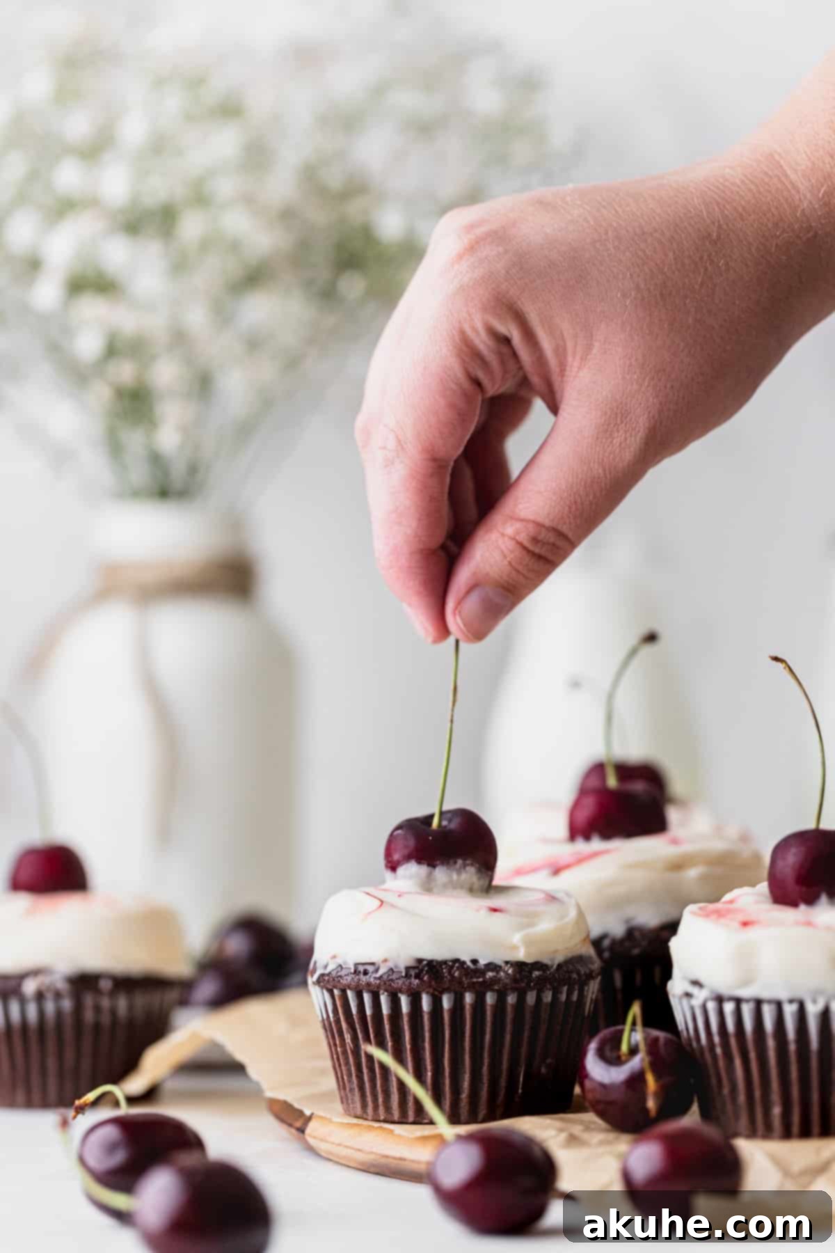 Decadent Black Forest Cupcakes 9 A hand gently placing a fresh cherry on top of a beautifully frosted Black Forest cupcake as a final decorative touch.