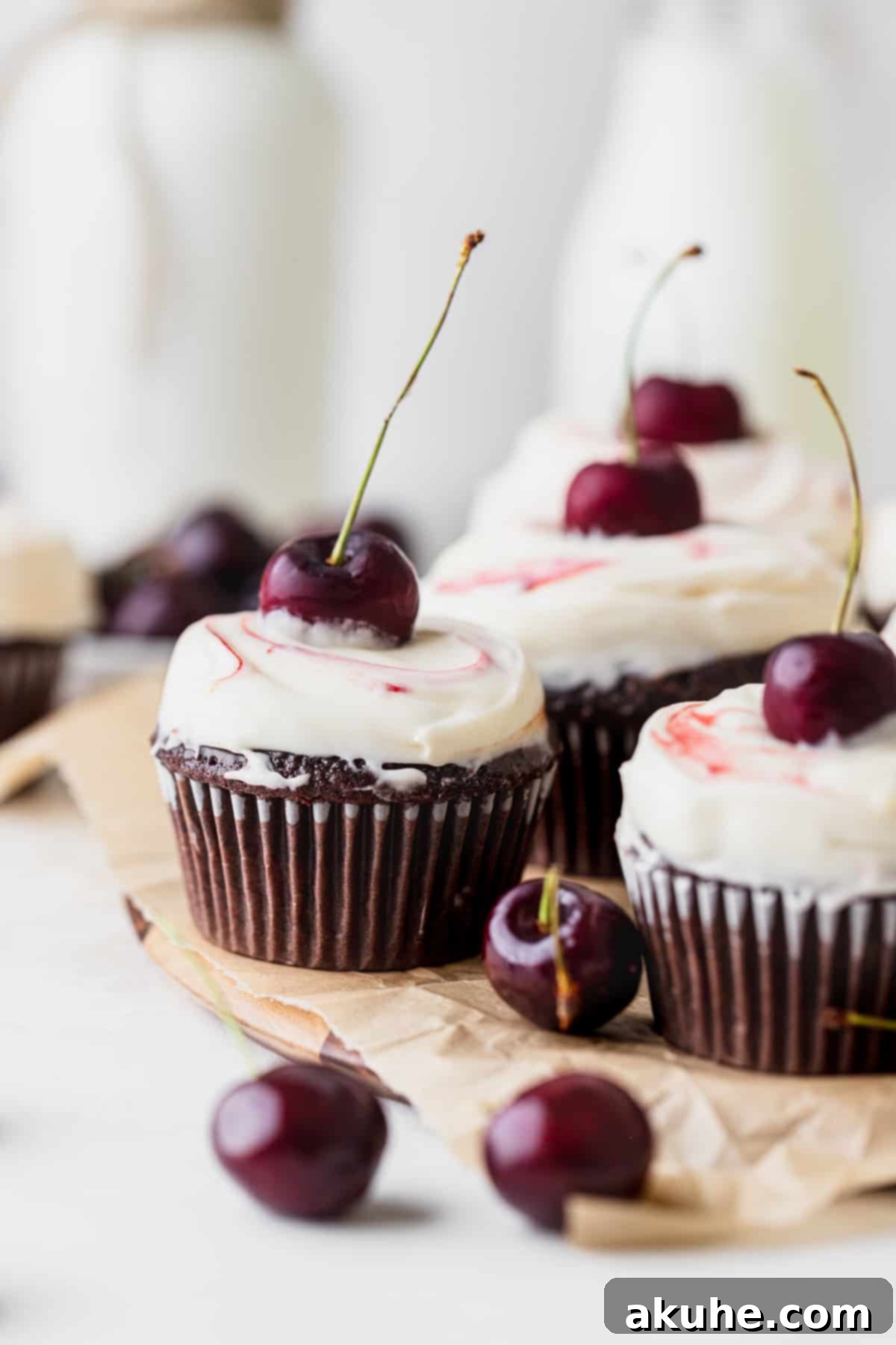 Decadent Black Forest Cupcakes 10 A collection of beautifully decorated Black Forest cupcakes, garnished with cherries and chocolate, arranged appealingly on a wooden board.